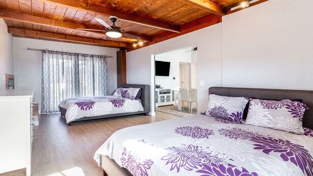 Un dormitorio con una cama grande, una cama más pequeña, un escritorio y un ventilador de techo.