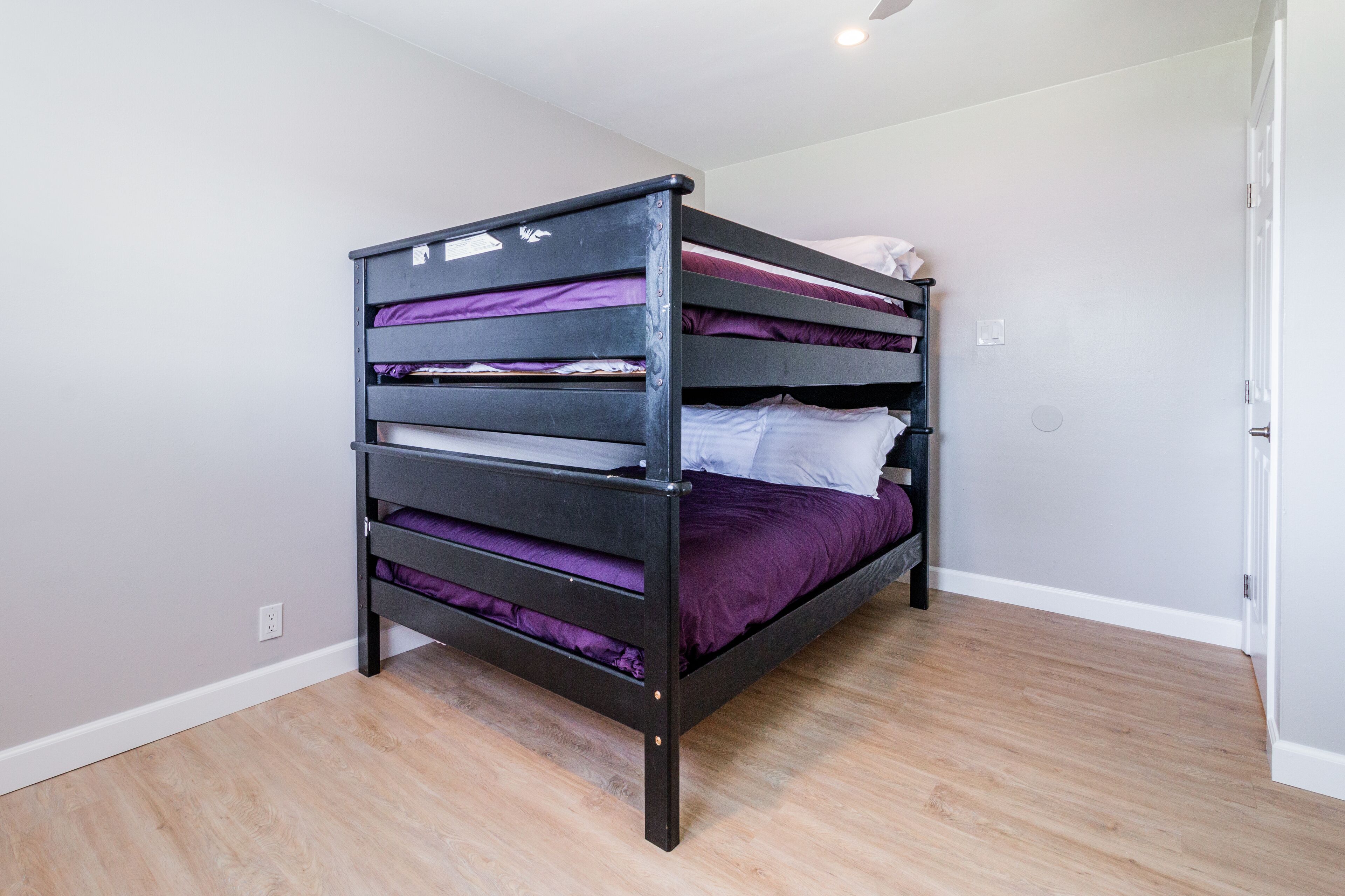 A bunk bed with multiple levels, a white door, and a light switch on the wall.