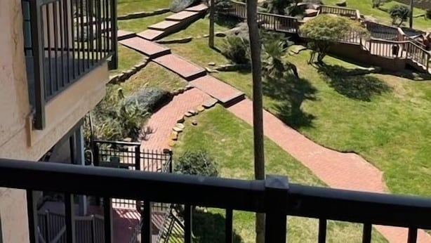 En balkon med udsigt over en strand, palmer og en belagt sti.