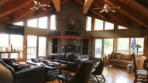 Un salón amplio con chimenea de piedra, mobiliario de cuero y ventanas grandes.