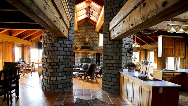 Un interior rústico con vigas de madera a la vista, una chimenea de piedra y una gran mesa de comedor de madera.