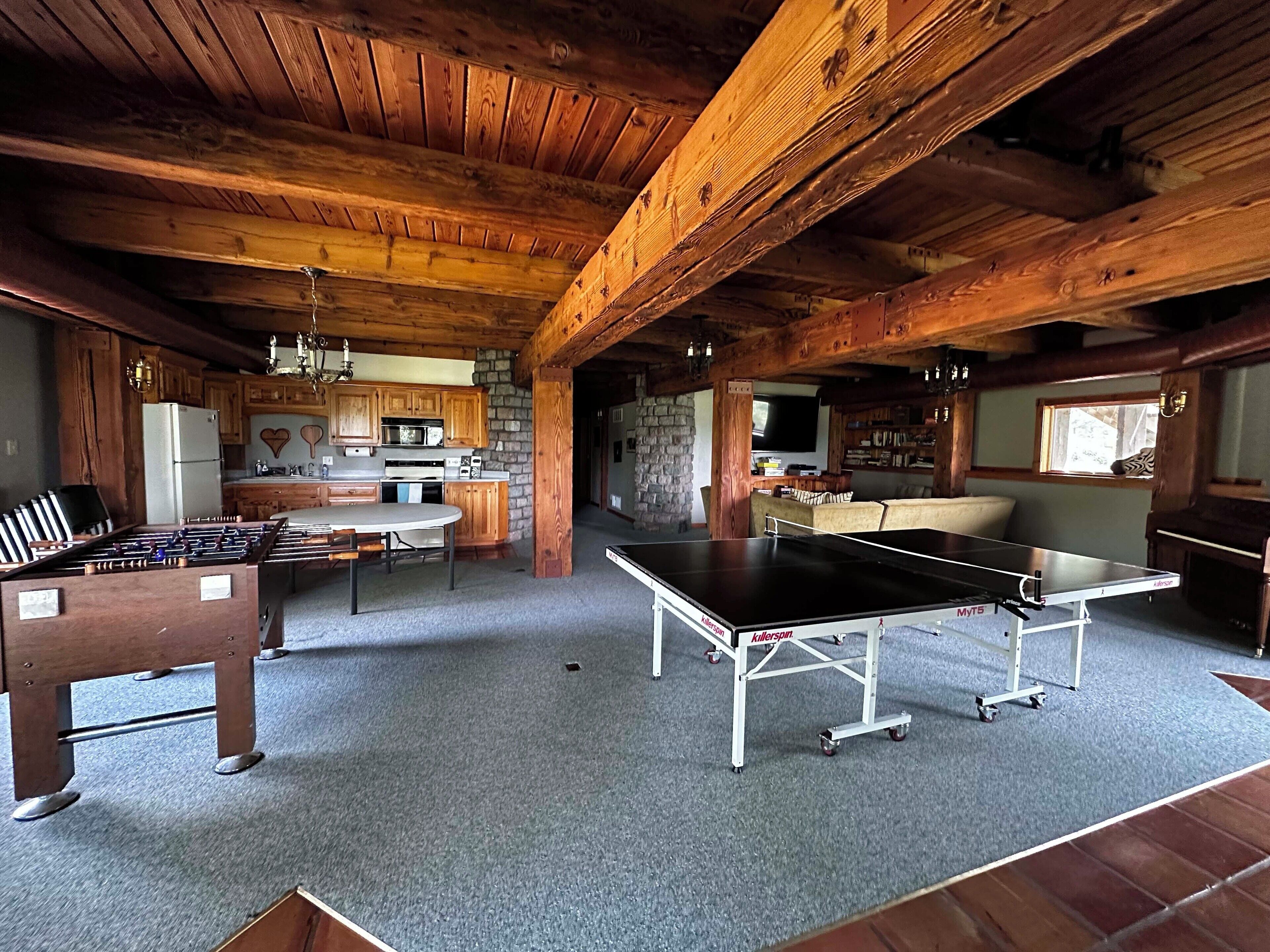 A rustic wooden interior with a kitchen, a foosball table, and a ping pong table.
