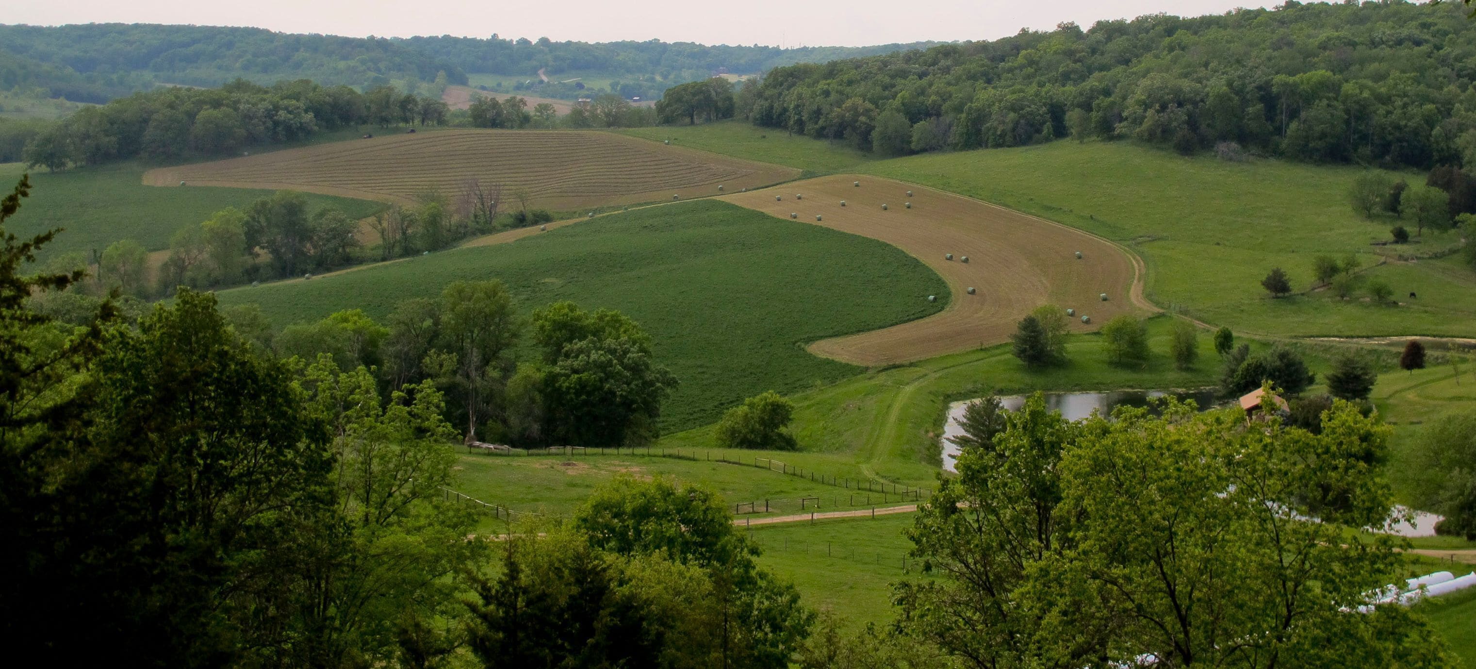 A rural landscape with fields, a winding road, and a small body of water.