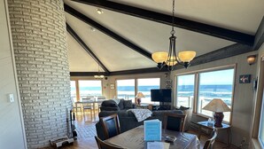Ein geräumiger Essbereich mit Holztisch und Stühlen, einer Kandelaber und Blick auf das Meer durch große Fenster.