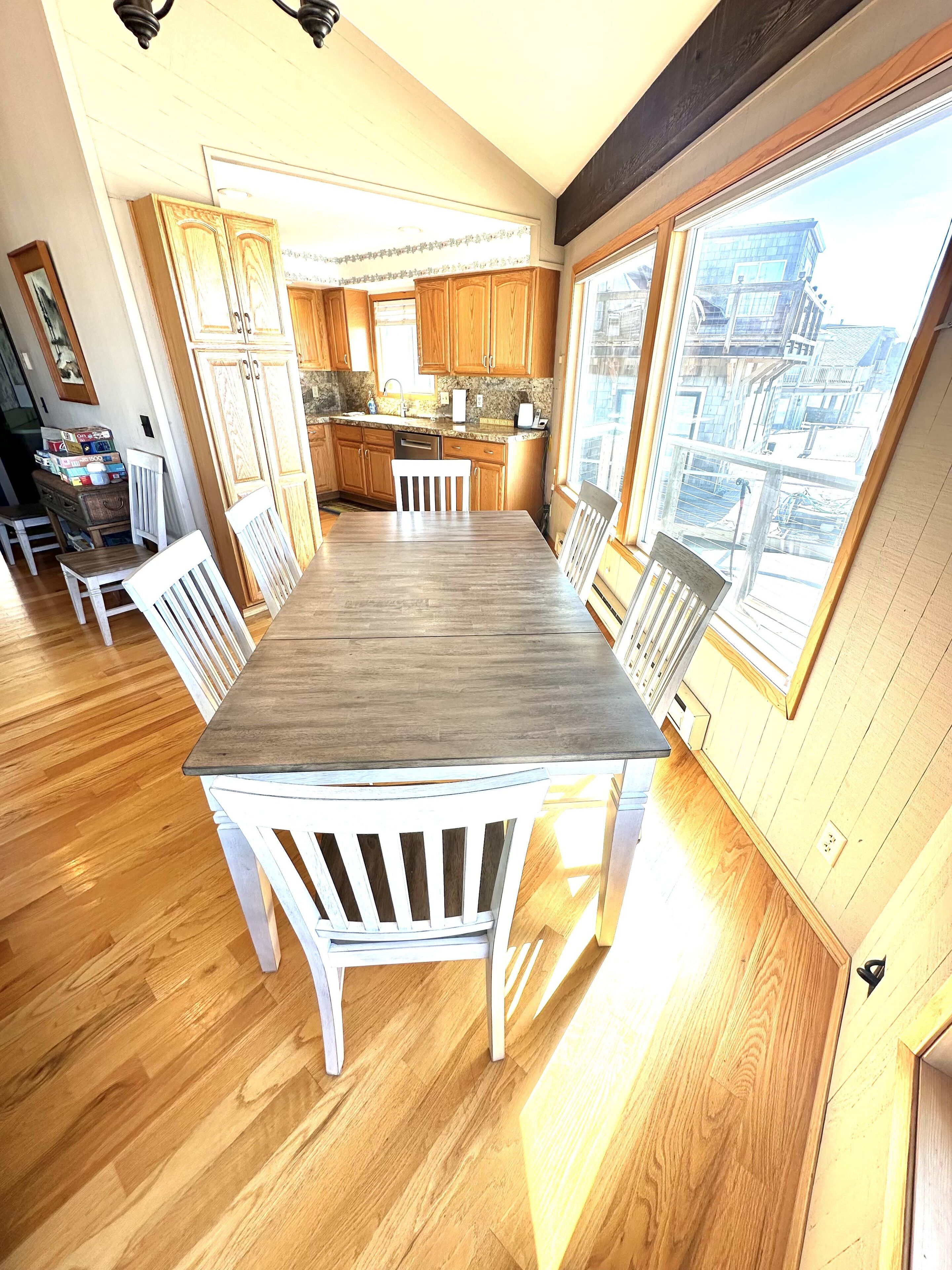 Une cuisine spacieuse avec des meubles en bois, une grande fenêtre et un coin repas comprenant une table en bois et des chaises blanches.