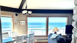 Ein großzügiger Wohnbereich mit großem Fenster zum Meer, einem Esstisch mit Stühlen, einer Couch und einer Lampe.