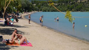 Una playa con gente tomando el sol y nadando, rodeada de vegetación y colinas.