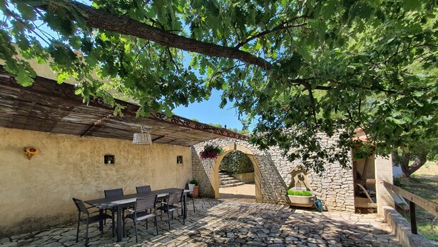 Un patio al aire libre con piso de piedra, pared de piedra rústica y una pérgola de madera.