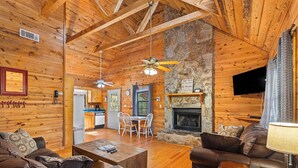 A cozy cabin interior with wooden walls, a stone fireplace, a dining area, and leather furniture.