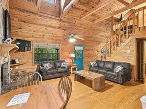A wooden cabin interior with two leather sofas, a dining table, a TV, and a staircase. - Country Charm B - Pet Friendly Cabin in city limits of Helen GA (Helen)
