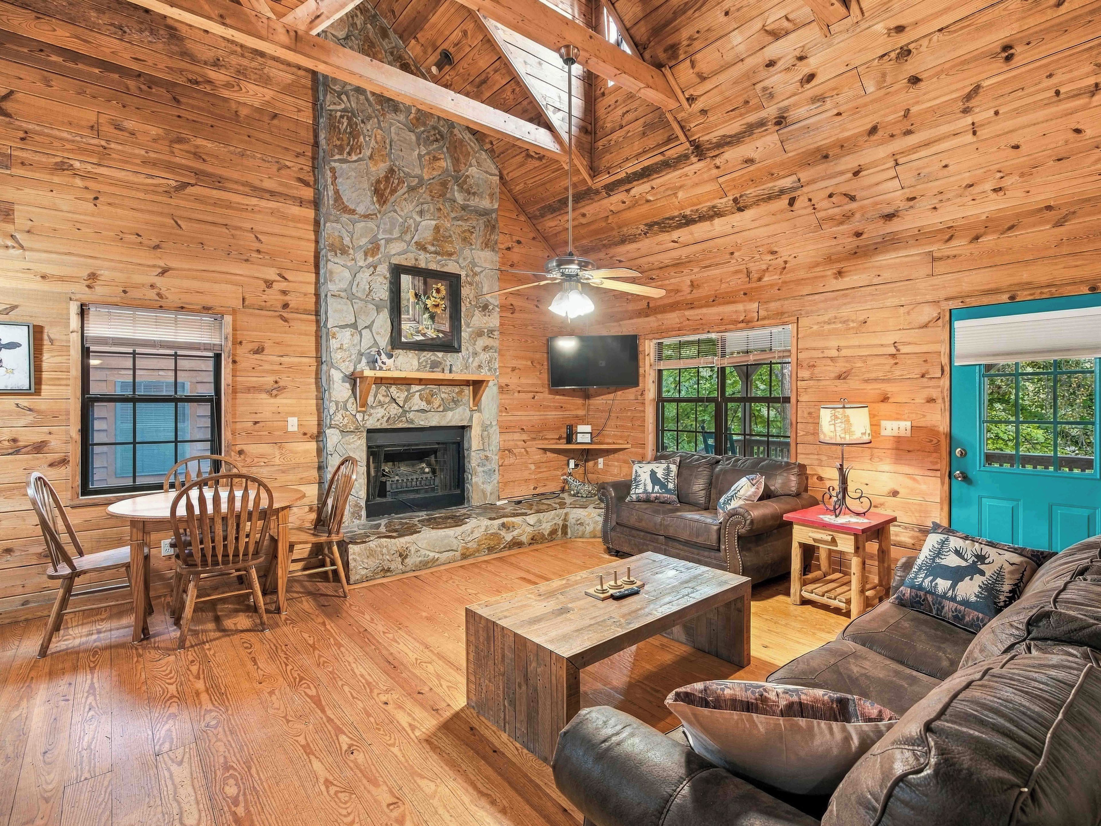 A log cabin interior with a stone fireplace, wooden furniture, and a television mounted on the wall.