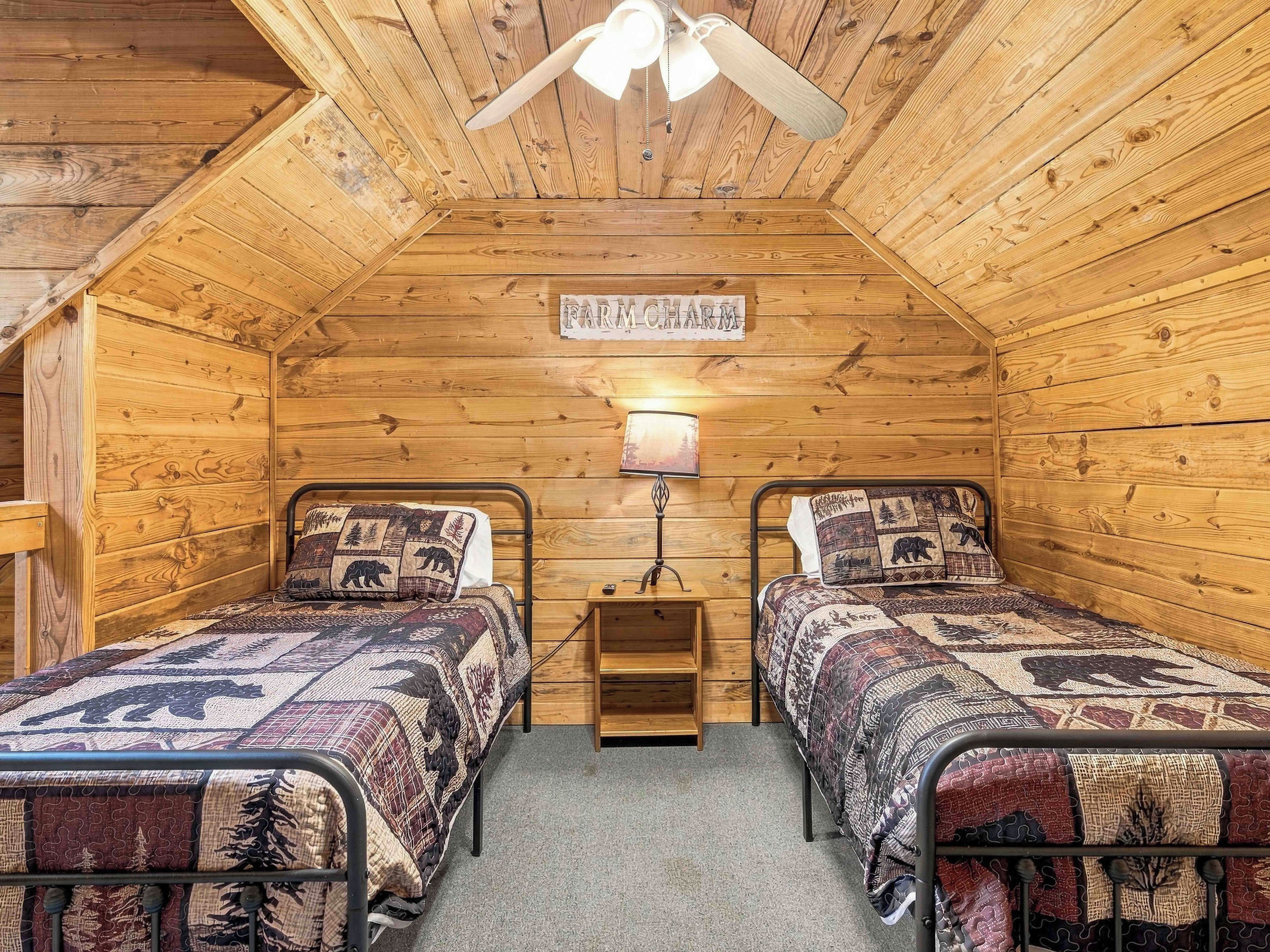 A cozy cabin room with two beds, a ceiling fan, and a sign reading 'FIND CHARM.'