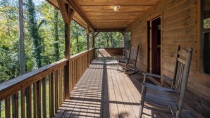 A wooden cabin with a covered porch, wooden railings, and a bench.