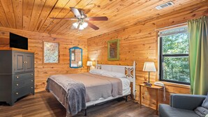A wooden cabin bedroom with a bed, dresser, and a window with curtains.