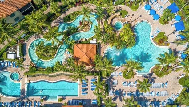 Vista aérea de um resort com várias piscinas, palmeiras e espreguiçadeiras.
