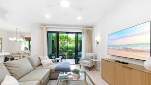 Uma sala de estar moderna com sofá, poltrona, mesa de centro, TV e uma varanda com área de estar externa.