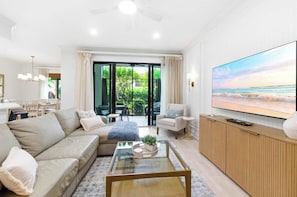 Ein modernes Wohnzimmer mit Sofa, Sessel, Couchtisch, Fernseher und einem Balkon mit Sitzgelegenheit.