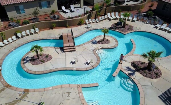 A large, curved swimming pool with multiple seating areas and palm trees. - PVZ105| Across Water Park * Pvt Hot Tub * Arcades (Santa Clara)