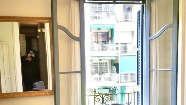 Quarto com uma mesa de vidro redonda, quatro cadeiras, um espelho e vista para uma varanda com guarda-corrimão.