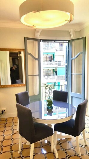 Quarto com uma mesa de vidro redonda, quatro cadeiras, um espelho e vista para uma varanda com guarda-corrimão.