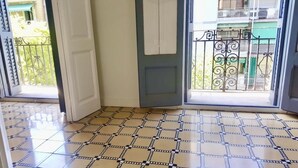 Quarto com soalho em azulejos, uma porta e vista para uma varanda com grade de metal.