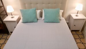 Cama bem arrumada com duas almofadas, cabeceira branca e duas luminárias de cabeceira em mesas de apoio combinando.