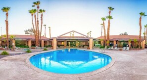 Un hotel con piscina central, palmeras y un patio cubierto.