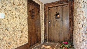 Een gang met een stenen muur en twee houten deuren, waarvan er één een metalen handgreep heeft en de ander een sleutelgat.