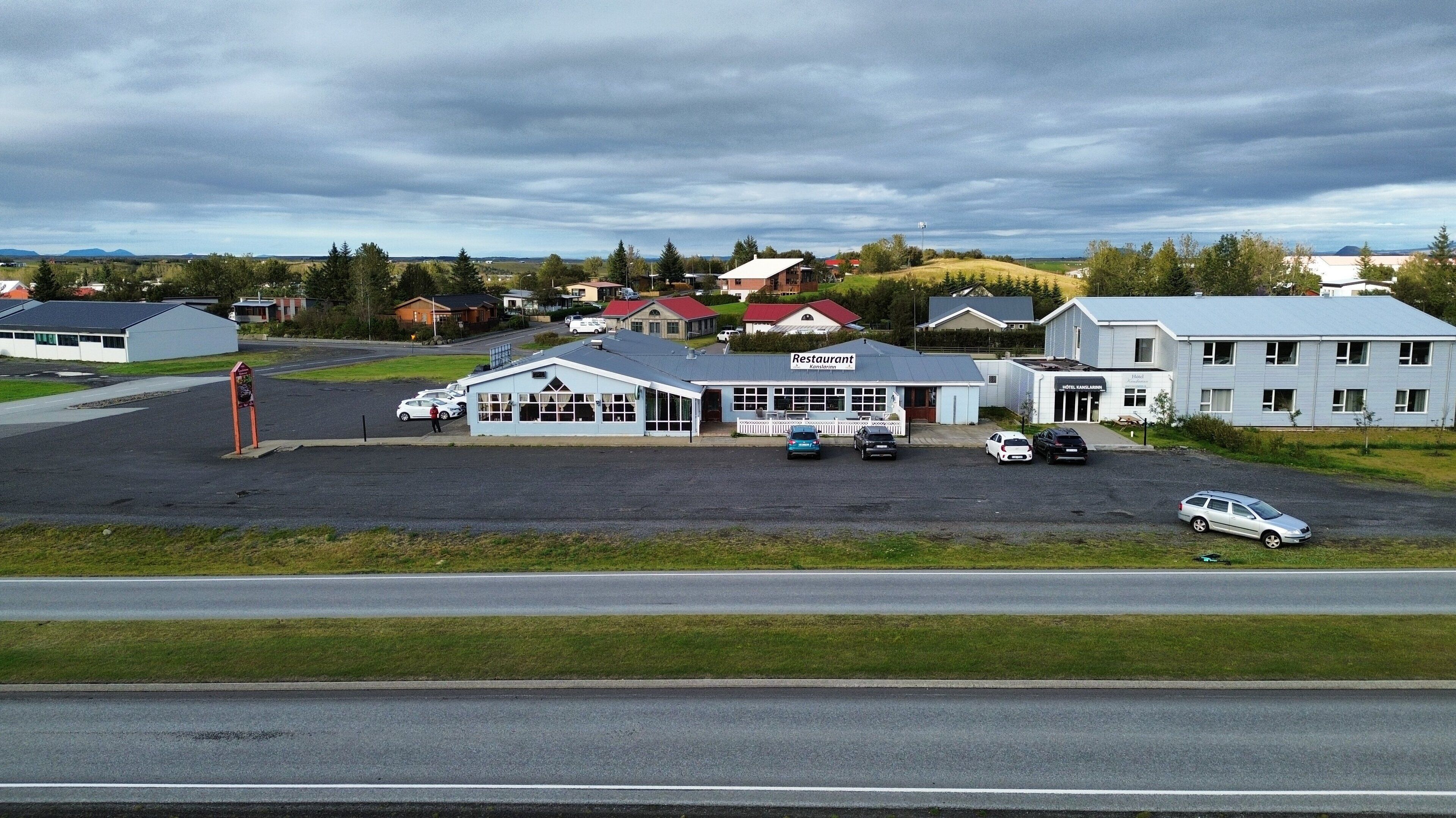 A building with a sign that reads "Restaurant" and "Hotel." There are cars parked in front, and a person walking.