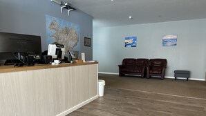 Ein Empfangsbereich mit Holztresen, einer Kaffeemaschine und einem Flachbildfernseher. Im Hintergrund befinden sich zwei Ledersofas und ein kleiner Tisch.