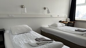 Ein Hotelzimmer mit zwei Einzelbetten, einem Schreibtisch mit Stuhl, einem Wasserkocher und einem Fenster mit Vorhängen.