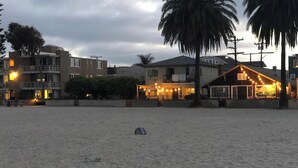 Una playa con edificios al fondo, incluyendo un restaurante con luces colgantes.