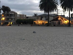 A beach with buildings in the background, including a restaurant with string lights.