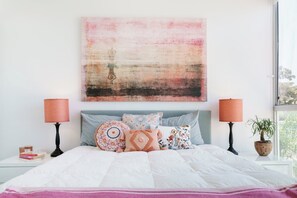 A bedroom with a bed, pillows, a nightstand, a lamp, and a window.