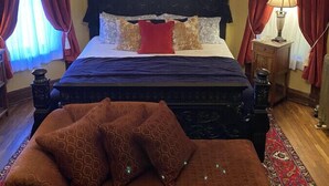 A bedroom with a large bed, a chandelier, red curtains, and a patterned rug.