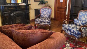 A room with a fireplace, two patterned armchairs, and a large, ornate wooden cabinet.