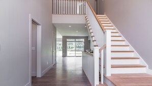 Ein modernes Interieur mit einer Holztreppe, einem Flur mit dunklem Holzboden und Blick auf eine Glastür, die nach draußen führt.