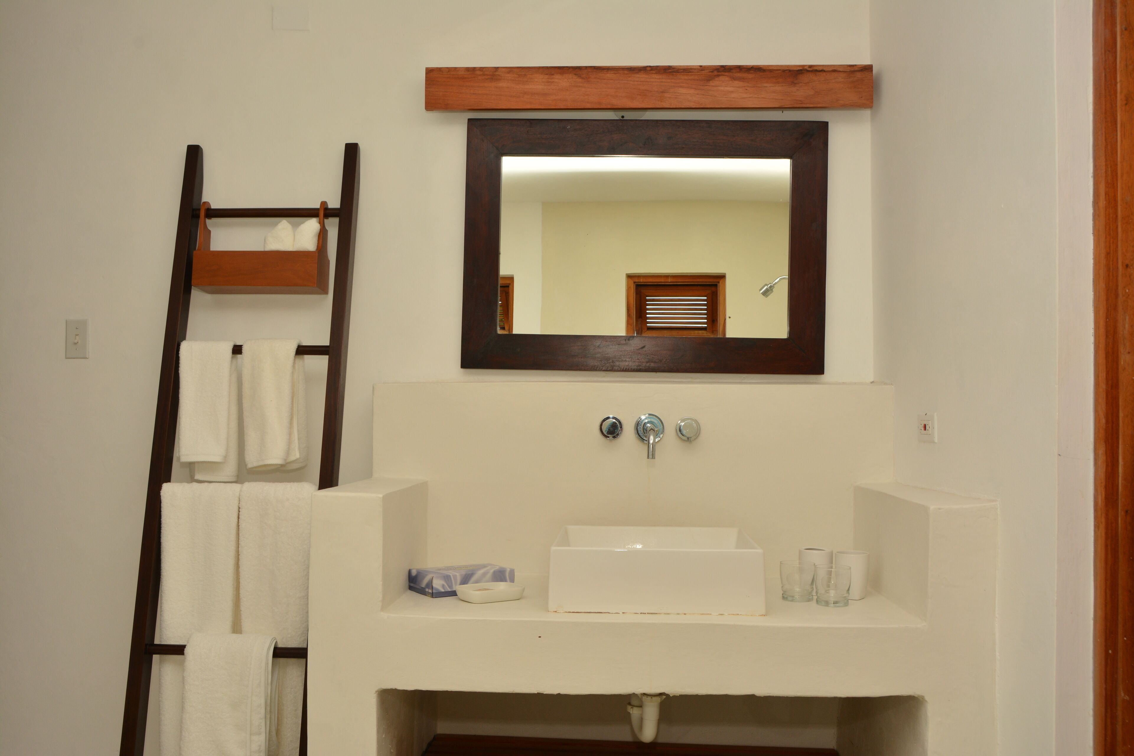 A bathroom with a white sink, two faucets, a mirror, and a towel rack with towels.
