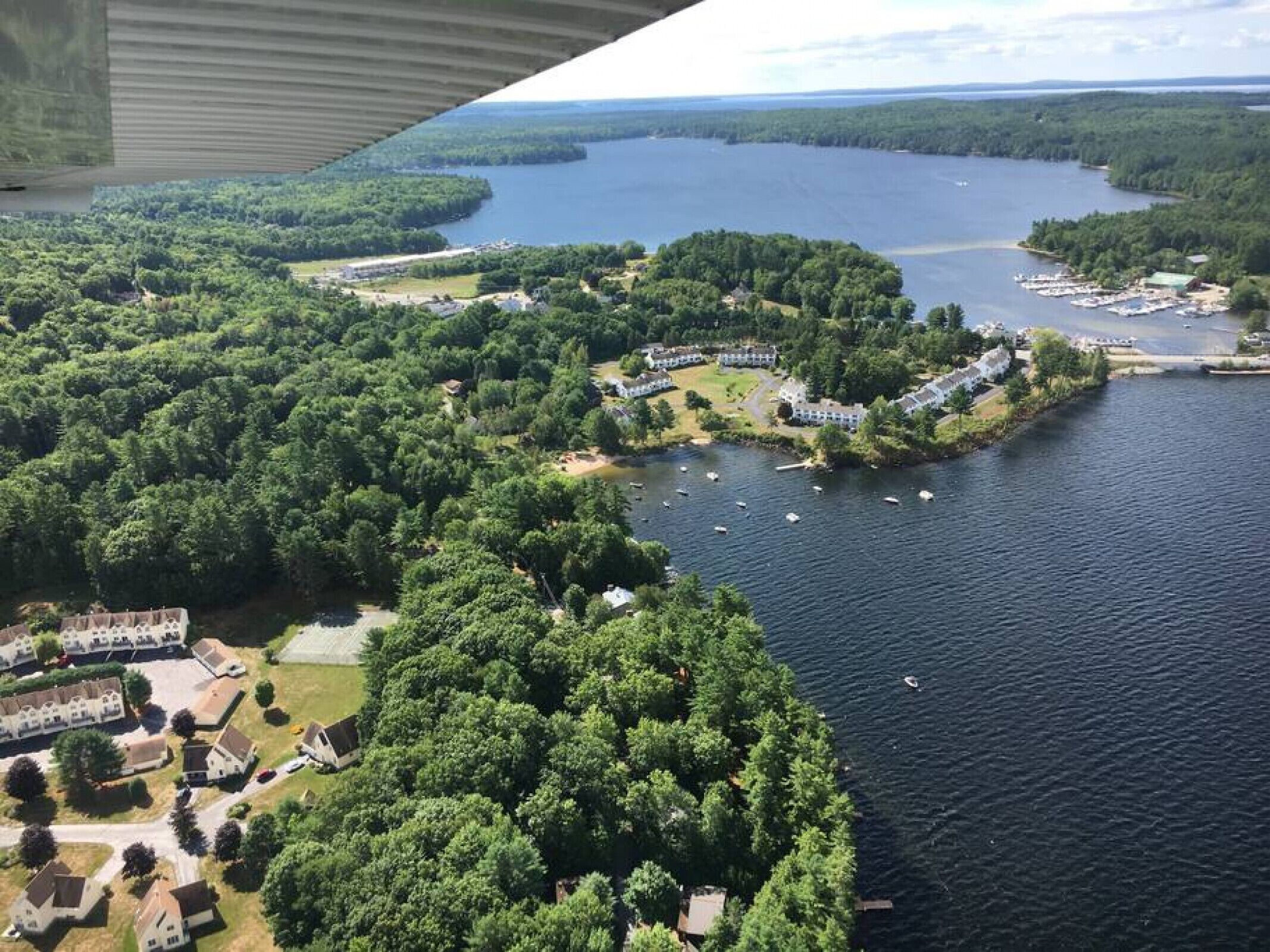 An aerial view of a lakeside property with multiple buildings, a marina, and lush greenery.