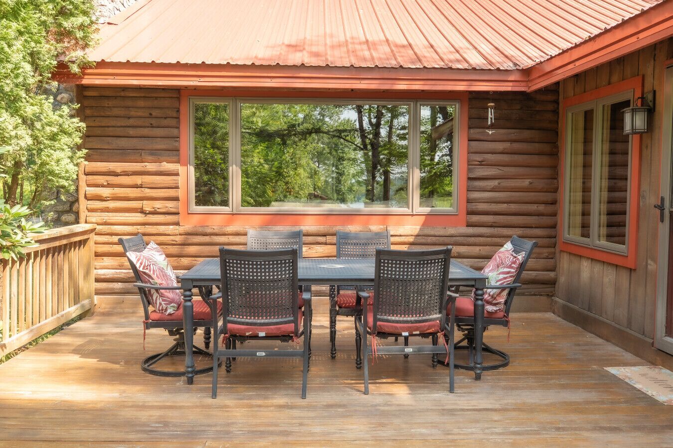 A wooden cabin with a deck, a table with chairs, and a window overlooking trees.