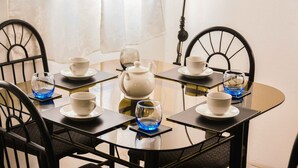 A round glass table with white teapots, cups, and saucers, surrounded by black chairs.