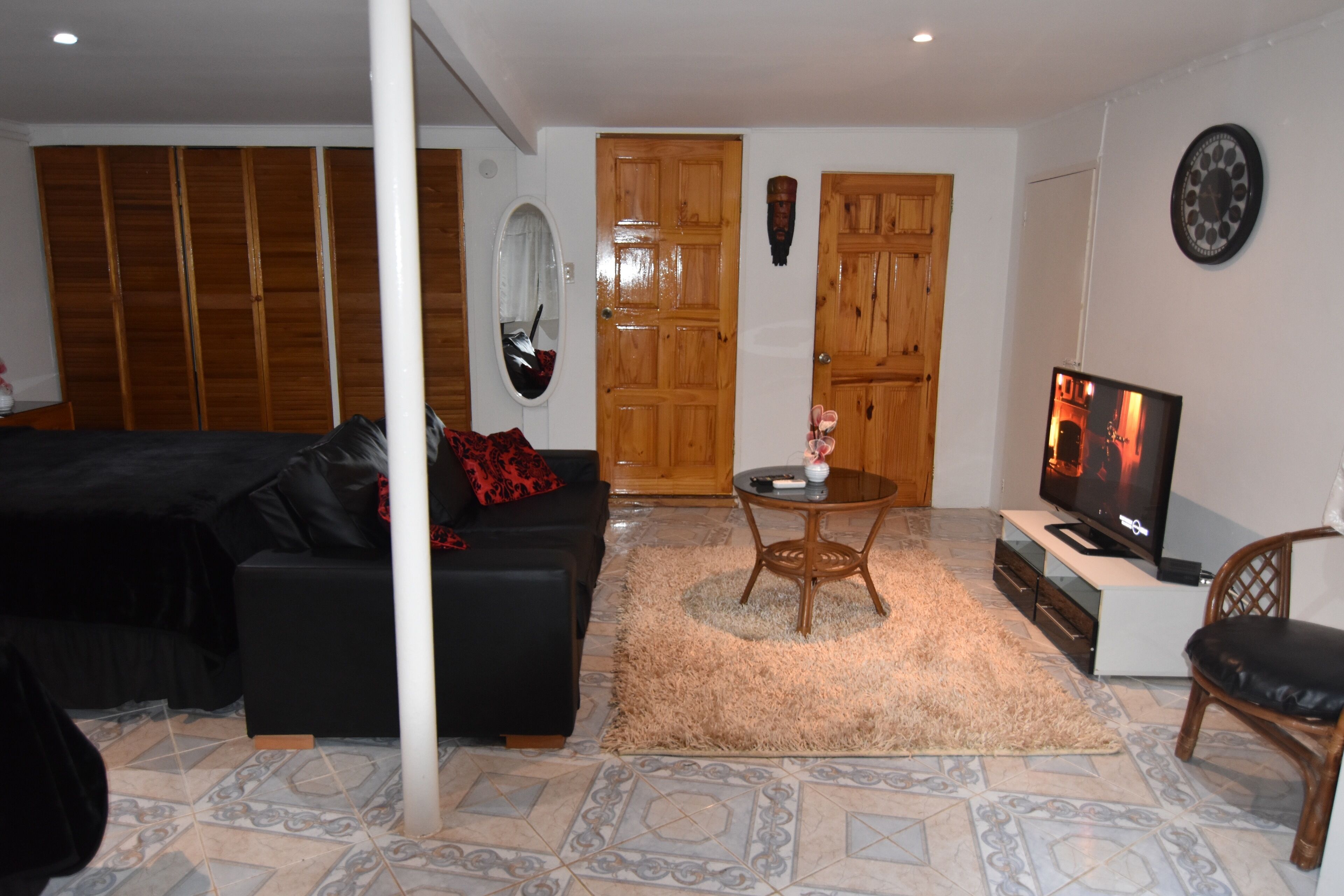 A living room with a black sofa, a wooden door, a television, and a mirror.