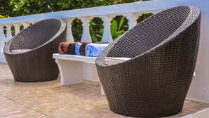 Two wicker lounge chairs with cushions, a bench, and a tiled floor.