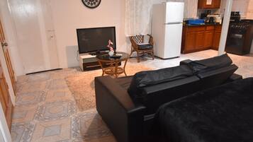 Un espacio habitable compacto con sofá, televisión, mesa de comedor y zona de cocina.