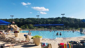 A swimming pool with lounge chairs and a slide, surrounded by trees and a clear sky.