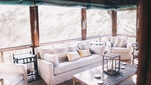 A cozy outdoor seating area with a sofa and chairs, a small table, and a view of trees through large windows.