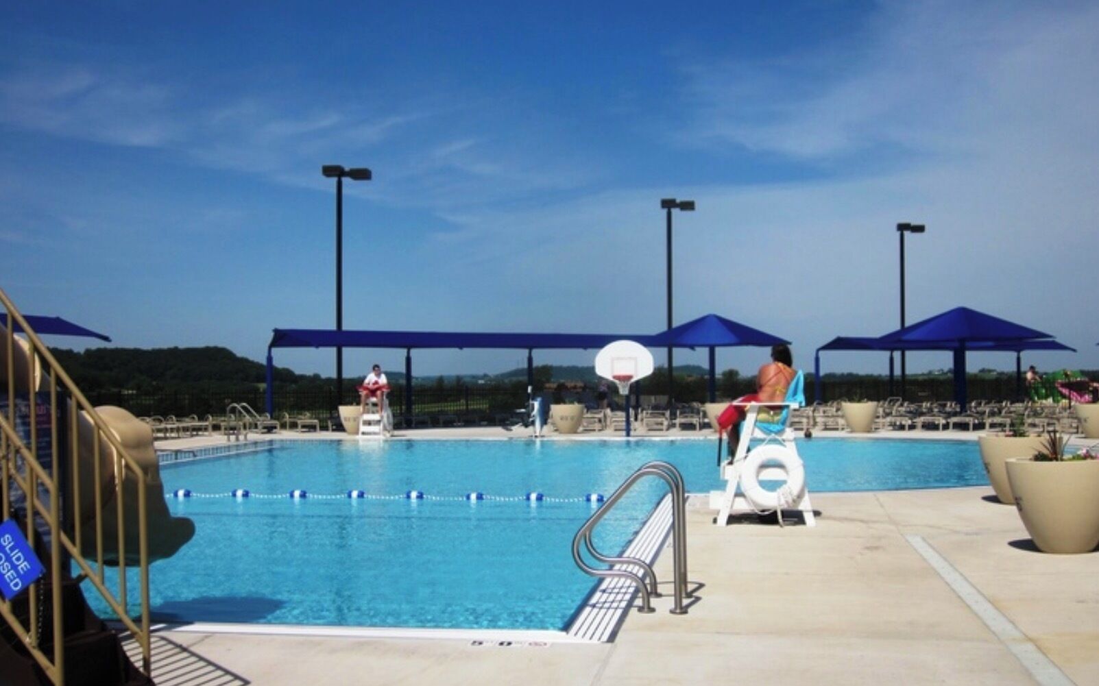 A swimming pool with diving boards, a basketball hoop, and lounge chairs.