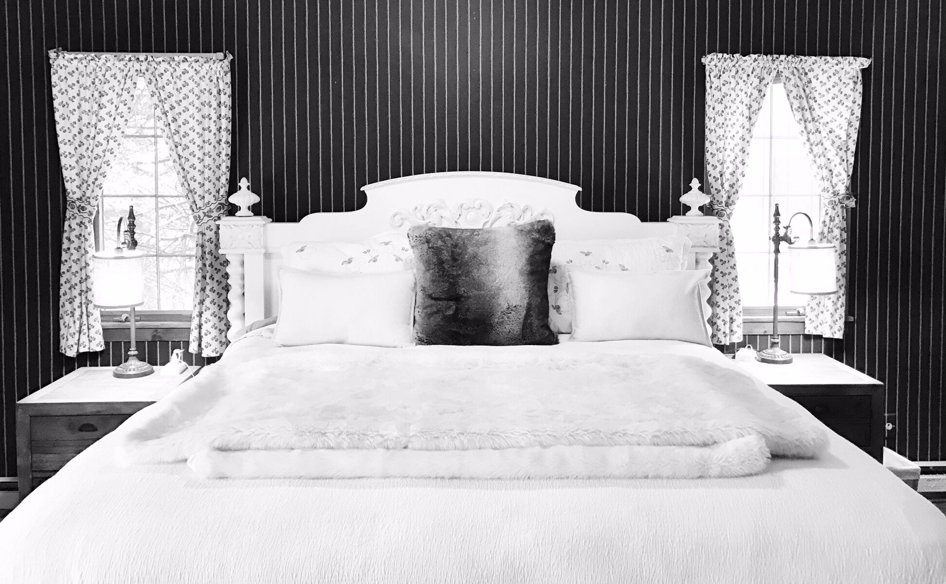 A bedroom with a large bed, floral curtains, and a nightstand with a lamp.