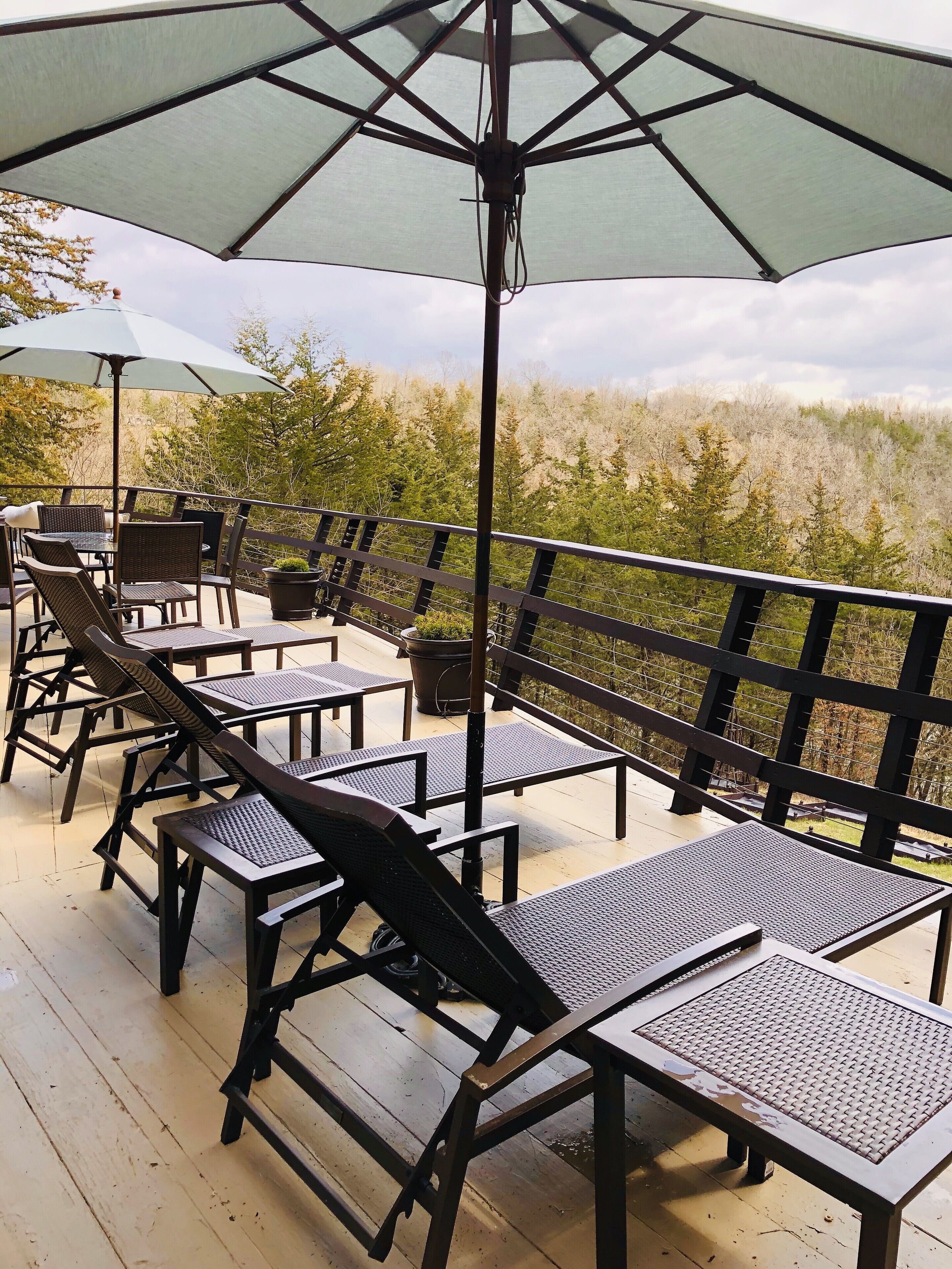 A deck with outdoor seating, including chairs and tables, and a large umbrella providing shade.