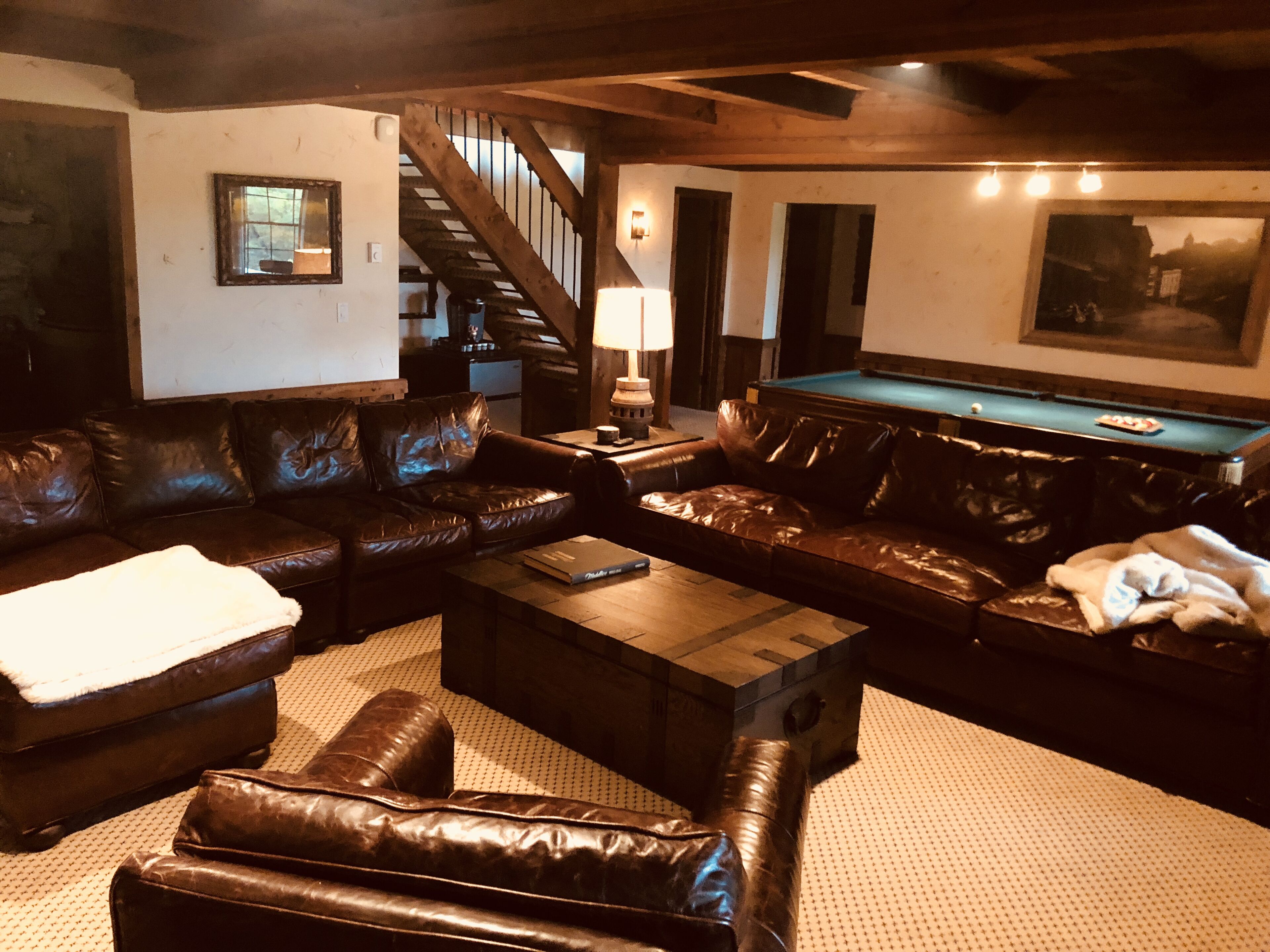 Un salon chaleureux avec des canapés en cuir, une table de billard et un escalier.